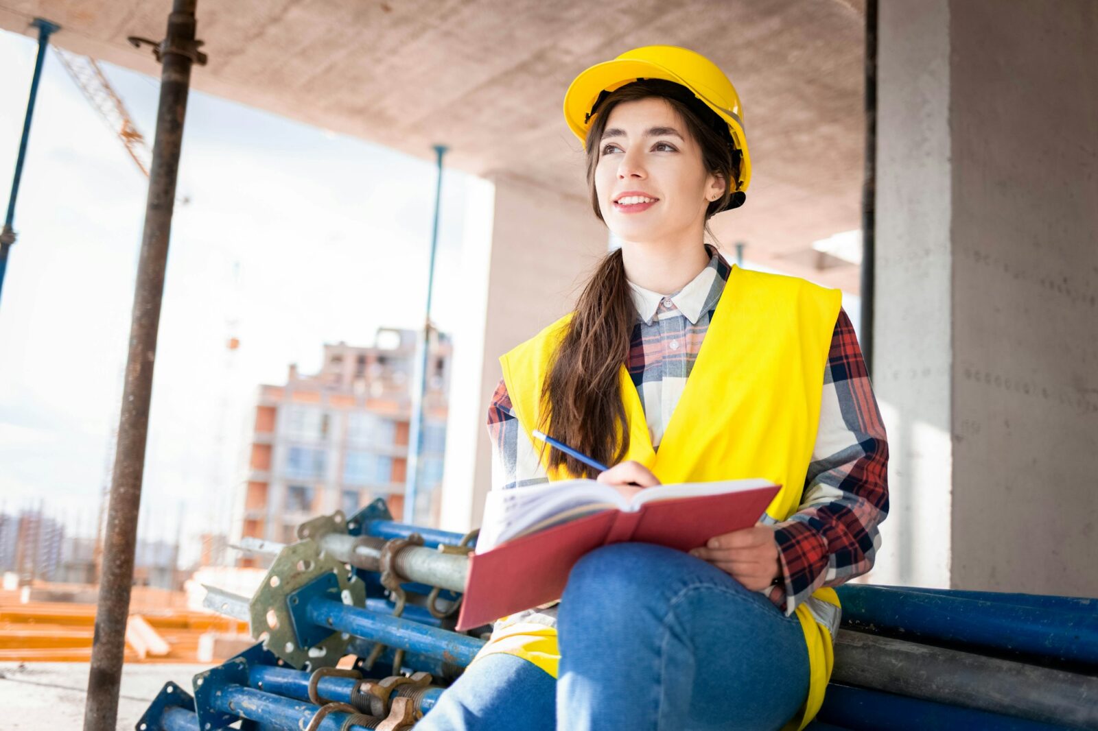 Girl in a construction helmet and vest writes in a notebook at a construction site