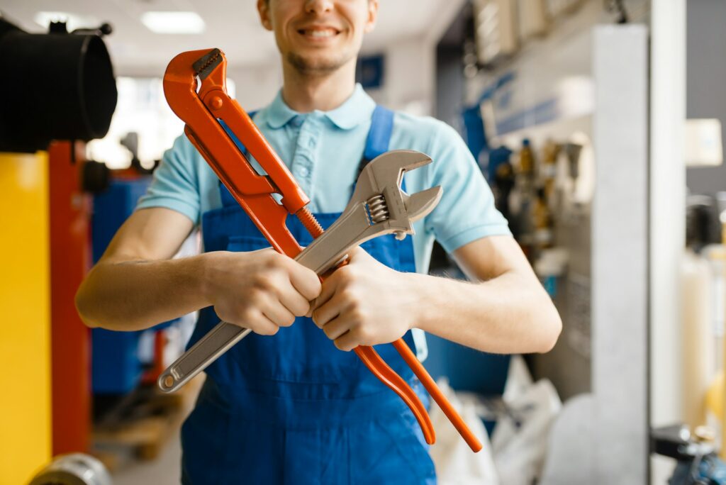 Plumber poses with pipe wrenches, plumbering store